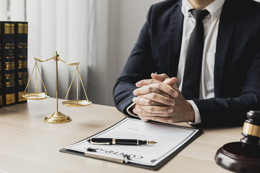 A male lawyer sits in the office of his law firm, on a table with a scale of justice and a hammer laying down, he is an attorney serving his client. Lawyer concepts and lawful justice.